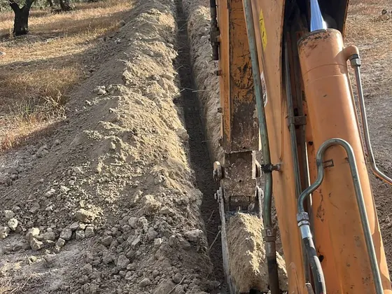 Pala y cilindros de una retroexcavadora dentro de una zanja recta en un olivar